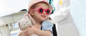 A girl wearing sunglasses shaped like flowers smiles and waits with her doctor nearby at Johns Hopkins All Children's Hospital.